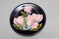 Front view of round ceramic plate showing pink floral decoration on dark blue background