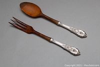 Full view of paired salad serving spoon and fork with sterling silver Rose Point handles and wooden ends.