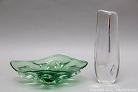 Clear tall blown glass vase and green sculptural bowl side by side on a neutral background.