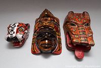 Front view of three hand carved and painted wooden masks showing detailed colors and designs of faces and headdresses.