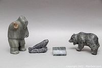 Photo showing all four Inuit stone carvings, including the large human figure missing an arm, seal, bear, and small rectangular piece.