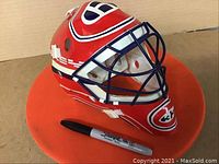 Side view of Montreal Canadiens goalie mask on an orange base with a Sharpie marker for scale.