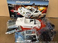 Playmobil Top Agents secret agent car white with black design partially assembled, figures and accessories still sealed in plastic bags, box in background with image and logo.