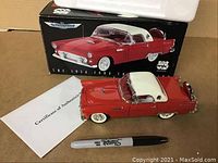 Red and white 1956 Ford Thunderbird diecast model next to original box and Certificate of Authenticity with a black Sharpie for size indication.