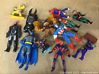 Photo of 13 assorted superhero action figures with some lying down and some standing, various colors and accessories visible.