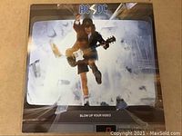 Front cover of AC/DC Blow Up Your Video album showing Angus Young jumping through broken screen