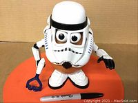 Front view of the Stormtrooper Mr. Potato Head figure with large eyes under the helmet, holding a blue accessory, posed on a surface with a Sharpie marker for size reference.