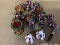 Photo showing 19 wooden eggs, 3 wooden egg cups with intricate painted designs, and 2 white porcelain egg-shaped salt and pepper shakers with red and black designs.