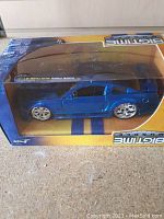 Photo of boxed blue Ford Mustang diecast model from Big Time Muscle series, showing side and top visible through clear plastic packaging.