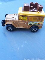 Side profile of the gold and yellow Majorette Toyota Safari die cast car showing the 'Raid Pekin Paris' decal and roof details.