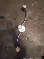 Metal 3-head LED light fixture on concrete floor showing curved arms and LED bulbs