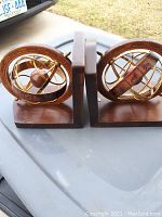 Two wood and brass globe-themed book ends seen from side view showing the armillary sphere design and base shape.