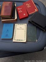 Top view of eight antique and scriptural books and booklets in various conditions, some leather-bound and others paper-covered, laid out on tray.