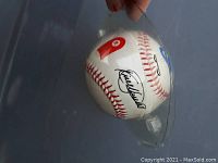 Photo showing a brand new baseball with signature and a red logo