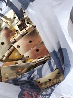 Top view of bag containing a collection of gold colored metal hinges and hardware pieces, showing varied hinge types and sizes with screw holes and knuckles.