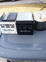 Photo of blank DVDs on spindle, adjacent new DVD cases stacked, and two Kool Krates storage crates (black and white) on a table outdoors.