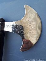 Close-up of the axe blade showing a reflective silver-toned surface with delicate engraved designs in dot patterns.