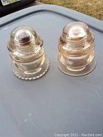 Photo of a pair of antique glass insulators placed on a gray surface outdoors.