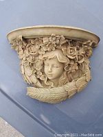 Front view of the garden shelf showing the female face with floral and leaf motifs sculpted in beige stone-like material.