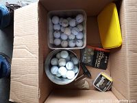 Box with two containers of golf balls, pack of golf spikes, magnetic ball retriever, assorted ball markers and tees, and a yellow zippered pouch.