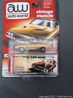 Photo of the 1:64 scale diecast model car of the 1973 Dodge Challenger in its original Auto World Vintage Muscle blister packaging. The packaging is intact and shows the branded red and black card with a photo of the car on the card text.