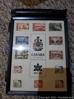 Display case with all 14 Canada Centennial stamps arranged neatly around a central card with the Canada Coat of Arms and Centennial text.