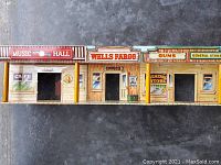 Front view of Marx Old West Town toy set showing Music Hall, Wells Fargo Office, Guns, and General Store facades with painted signs and window openings