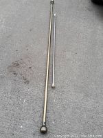 Long and short metal curtain rods displayed on concrete floor, showing extendable feature on the longer rod and finial designs.
