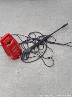 Photo showing red electric pressure washer and attached black spray gun on concrete surface