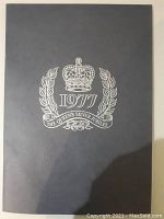 Dark blue cover of the 1977 Silver Jubilee stamp book with embossed silver crown, laurel wreath, and text