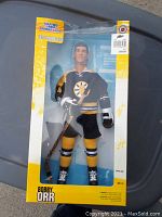 Front view of the vintage Bobby Orr action figure in packaging. Figure is dressed in Boston Bruins uniform holding a hockey stick.