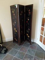 Room divider positioned in corner showing full three hinged panels with floral designs.