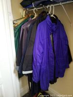Seven ladies coats hanging on a closet rod with white plastic hangers