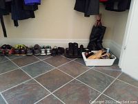 Wide angle shot of multiple shoes and boots lined along a wall with a white tray containing shoe care products to the side and a black hat on a mannequin in the corner.