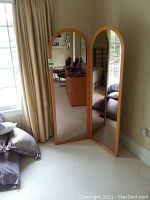 Full view of two-panel mirror standing open in room, showing wood frame and arched mirror tops.