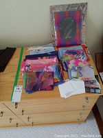 Wide view of twelve folded silk scarves and packaging materials on a wooden cabinet