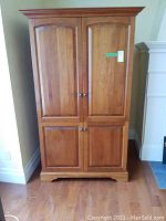 Front view of the wooden cabinet with closed four paneled doors, showing medium brown wood finish.