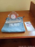 Full view of Waterford crystal mantel clock resting on branded Waterford soft pouch on wooden surface, with auction lot tag beside it.