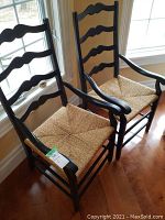 Front view of two ladder back armchairs with rush seats and black frames