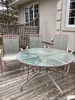Overall view of round glass-top table and four sling chairs on wooden deck