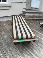 Full view of wooden lounger with striped cushion outdoors on wood deck, backrest adjusted upright.