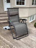 Angle view of grey anti gravity chair with attached side table positioned on wooden deck.
