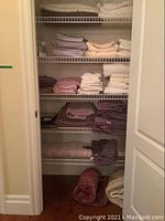 Closet shelves stacked with multiple folded bath towels in pastel colors and neutrals, along with blankets and bedding below