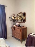 Full view of the dresser and matching mirror on the wall in a room with curtains and carpeted floor.