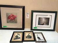 Five framed art prints on a table including a floral print, a winter road photo print, and three smaller bird prints.