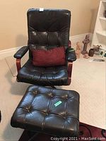 Black leather swivel chair with wooden armrests and matching ottoman. Chair shows visible wear and creases on seat.
