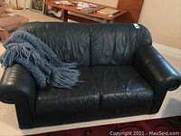 Full view of black leather loveseat with grayish-blue throw on one side, showing overall condition and size.