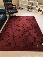 Full view of burgundy area rug with black vine scroll design in a room setting.