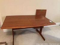 Front view of rectangular teak table with leaf displayed upright at end.