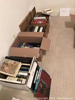 Overview of boxes filled with various art, history, and photography books, some larger hardcovers set outside the boxes.
